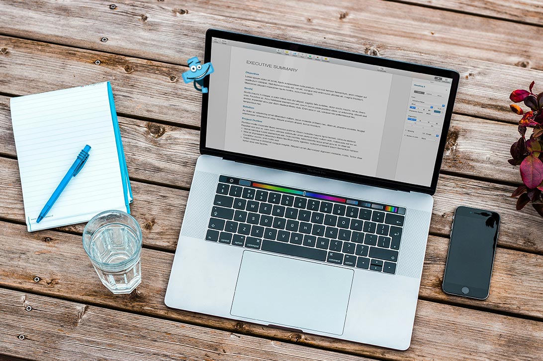Leżący na biurku laptop, obok niego notes, telefon i szklanka wody