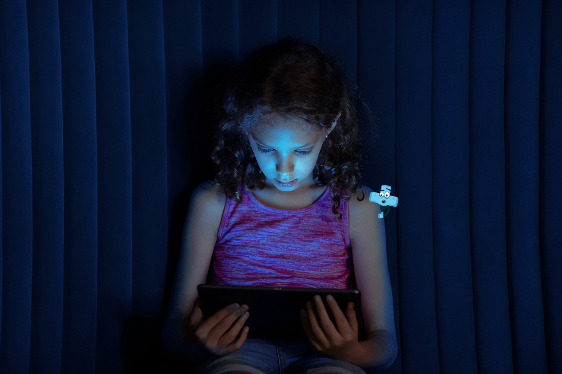 Dziewczynka siedzi, w rękach trzyma tablet i coś na nim ogląda.