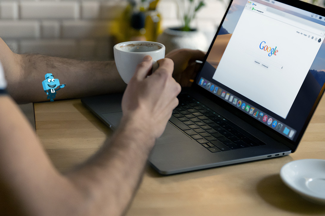 Osoba z kawą w dłoni siedząca przed laptopem z otwartą wyszukiwarką Google